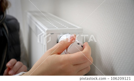 Closeup of woman adjusting heating radiator thermostat and warming her hands. Concept of energy crisis, high bills, broken heating system, economy and saving money on monthly utility payments. Closeup of woman adjusting heating radiator thermostat and warming her hands. Concept of energy crisis, high bills, broken heating system, economy and saving money on monthly utility payments. 106209121