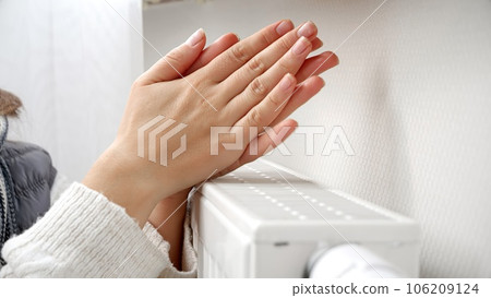 Closeup of woman feeling col warming her hands at wall heater 106209124