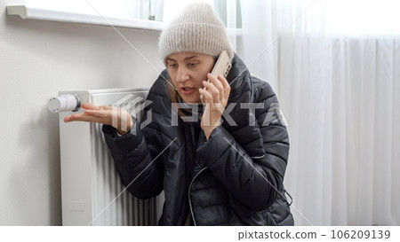 Young woman in warm clothes speaking to tecnician by phone about broken heater or radiator Young woman in warm clothes speaking to tecnician by phone about broken heater or radiator 106209139