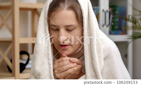 Young woman feeling cold at home covering in duvet and breathing on freezing hands Young woman feeling cold at home covering in duvet and breathing on freezing hands 106209153