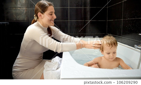 Happy smiling mother looking at her baby son relaxing and washing in bath at home. Concept of parenting, happiness and child hygiene. 106209290