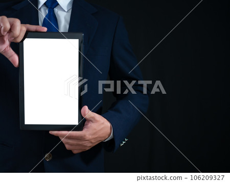Businessman standing holding white screen tablet on dark background. Advertising concept. Banner sign. Businessman standing holding white screen tablet on dark background. Advertising concept. Banner sign. 106209327