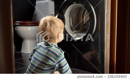 Cute smiling baby boy looking at spinning clothes in washing machine. Doing housework and chores, children education and development. 106209405