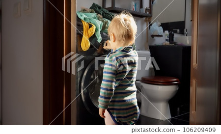 Little baby boy pressing knobs and buttons on working washing machine. Doing housework and chores, children education and development. Little baby boy pressing knobs and buttons on working washing machine. Doing housework and chores, children education and development. 106209409