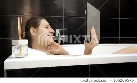 Woman taking a bath while staying connected with friends and family via a video call on her tablet computer. Authenticity and promoting the importance of social interaction. Woman taking a bath while staying connected with friends and family via a video call on her tablet computer. Authenticity and promoting the importance of social interaction. 106209570