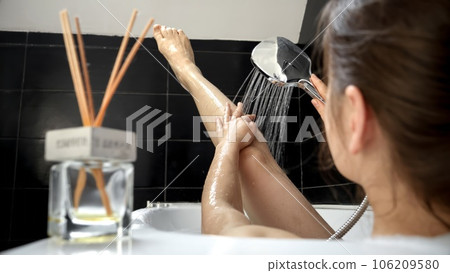 A woman enjoying a refreshing bath, taking care of hygiene by washing her legs under a gentle shower - a perfect way to promote overall wellness and beauty 106209580