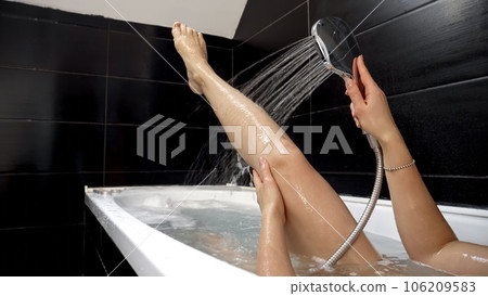 Closeup of woman washing legs under shower while lying in bath. Female hygiene, relaxing in bathroom, beauty and health. 106209583