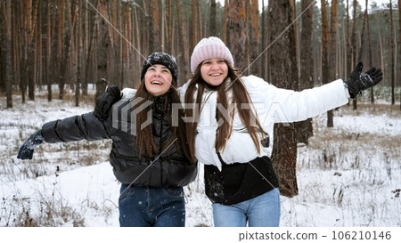 Two laughing teenage girls cheering and laughing while catching falling snowflakes in winter forest Two laughing teenage girls cheering and laughing while catching falling snowflakes in winter forest 106210146