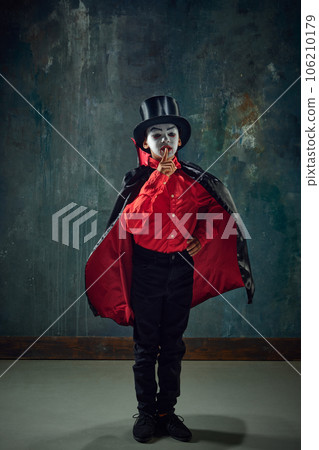 Shh. Keeping secret. LLittle boy, child in image of creepy vampire wearing costume and makeup against vintage green background Shh. Keeping secret. LLittle boy, child in image of creepy vampire wearing costume and makeup against vintage green background 106210179