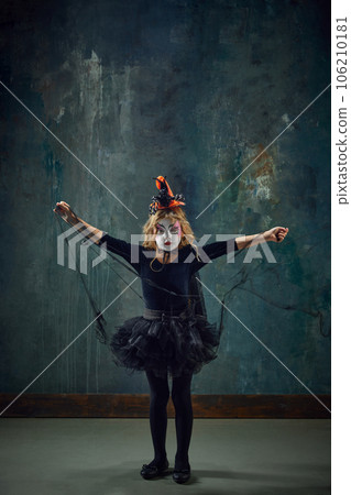 Little girl, child in i witch costume, with creepy makeup standing against dark vintage background. Spooky look 106210181