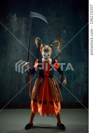Little girl, child in costume and makeup for halloween party standing with frightening face against dark vintage background 106210207