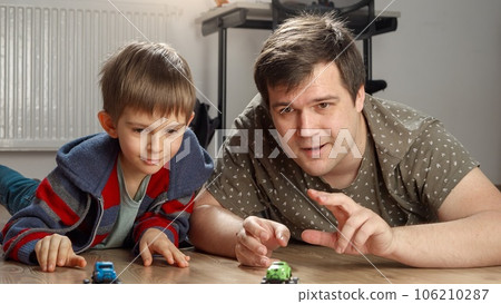 Young father and boy having toy car race on floor in bedroom. Children playing alone, development and education, games at home. 106210287