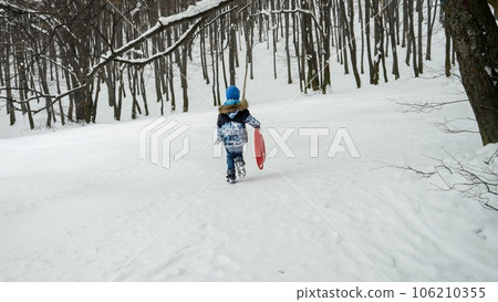 Happy boy is carrying his plastic sleds up the hill, excited for the snow and all the outdoor activities it brings during the winter season. Happy boy is carrying his plastic sleds up the hill, excited for the snow and all the outdoor activities it brings during the winter season. 106210355