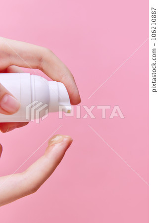 Close up image of female hand squeezing cream, gel for hands from unmarked bottle with dispenser on finger on pastel pink background. Close up image of female hand squeezing cream, gel for hands from unmarked bottle with dispenser on finger on pastel pink background. 106210887
