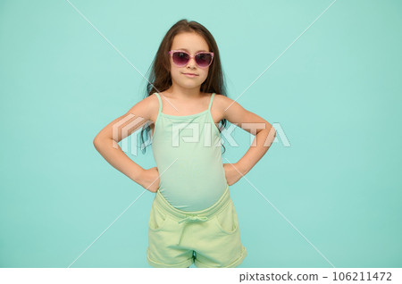 Mischievous child girl in summer clothes, putting hands on her waist, looking at camera, isolated blue studio background Mischievous child girl in summer clothes, putting hands on her waist, looking at camera, isolated blue studio background 106211472