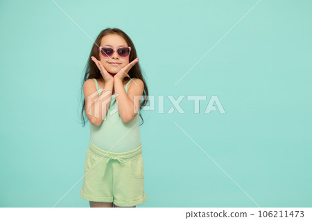 Lovely little girl holding her face with her hands, looking at camera, isolated on blue studio background. Copy ad space Lovely little girl holding her face with her hands, looking at camera, isolated on blue studio background. Copy ad space 106211473