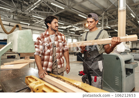 Two young carpenters working with wood standing at table in workshop Two young carpenters working with wood standing at table in workshop 106212653