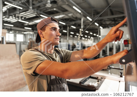Young carpenter operating machine for wood processing at a furniture factory 106212767