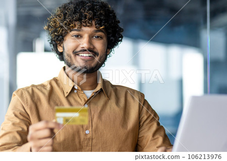 Portrait of young successful hispanic businessman inside office, man smiling and looking at camera, entrepreneur holding bank credit card in hands, satisfied with results of money transfer. Portrait of young successful hispanic businessman inside office, man smiling and looking at camera, entrepreneur holding bank credit card in hands, satisfied with results of money transfer. 106213976