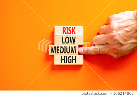 Time to medium risk symbol. Concept word Risk low medium high on wooden block. Businessman hand. Beautiful orange table orange background. Business time to medium risk concept. Copy space. Time to medium risk symbol. Concept word Risk low medium high on wooden block. Businessman hand. Beautiful orange table orange background. Business time to medium risk concept. Copy space. 106214802