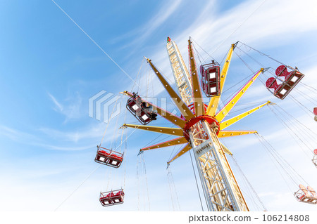 Scenic bottom view high chain swing flying carousel against blue sky. Merry go round roundabout chairoplane at portable amusement park. People enjoy having family fun play riding at fair festival 106214808