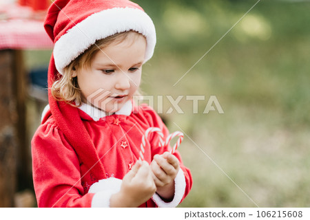 Christmas in july. Child waiting for Christmas in wood in summer. portrait of little girl in red dress decorating christmas tree. winter holidays and people concept. Merry Christmas and Happy Holidays Christmas in july. Child waiting for Christmas in wood in summer. portrait of little girl in red dress decorating christmas tree. winter holidays and people concept. Merry Christmas and Happy Holidays 106215608