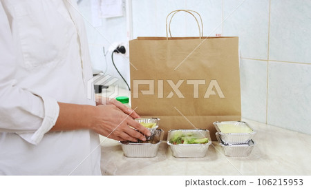 Food delivery service in restaurant. Chef packs lunch boxes to paper bag. Healthy diet daily menu, food meal dishes in a plastic takeaway containers. Woman cook on white kitchen collecting food box 106215953