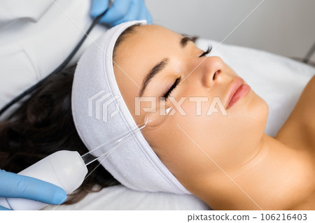 Specialist makes hardware vacuum facial massage to lady client. Effect of smoothness and cleanliness of woman body part. Spa service concept 106216403