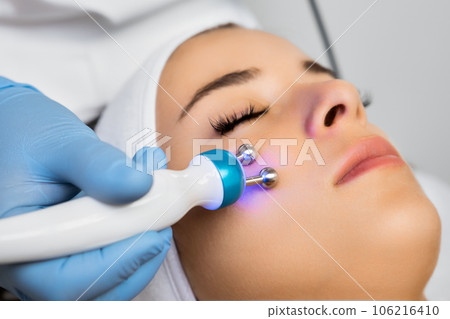 Specialist in rubber gloves uses microcurrent massage device on female face. Method of influencing body with modulated pulses concept Specialist in rubber gloves uses microcurrent massage device on female face. Method of influencing body with modulated pulses concept 106216410