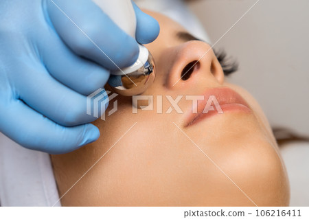 Close up expert applies hardware face massage for rejuvenation to beautiful woman. Close up expert applies hardware face massage for rejuvenation to beautiful woman. 106216411