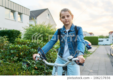 Schoolgirl child 10, 11 years old with backpack on bicycle on street near house 106217656