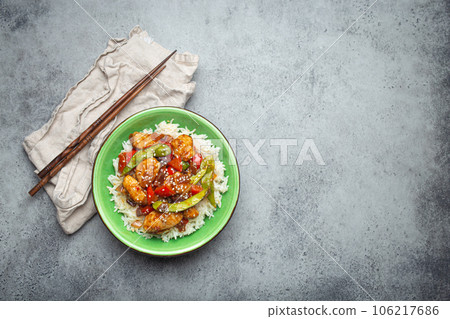 Asian sweet and sour sticky chicken with vegetables stir-fry and rice in ceramic bowl with chopsticks top view on gray rustic stone background, traditional Asian dish. Copy space 106217686