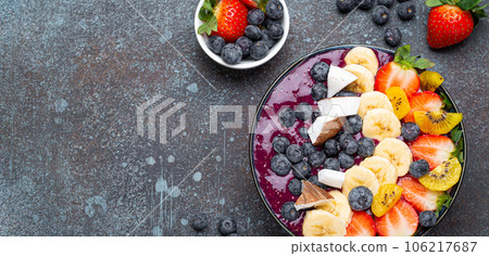 Healthy summer acai smoothie bowl with chia seeds, fresh banana, strawberry, blueberry, cocos, kiwi top view, rustic concrete background with spoon. Copy space 106217687