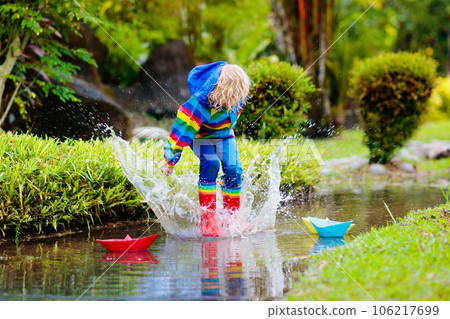 Child with paper boat in puddle. Kids by rain. Child with paper boat in puddle. Kids by rain. 106217699