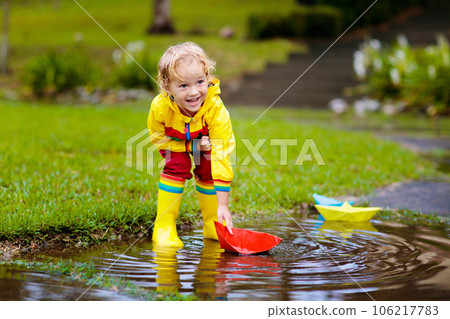 Child with paper boat in puddle. Kids by rain. 106217783