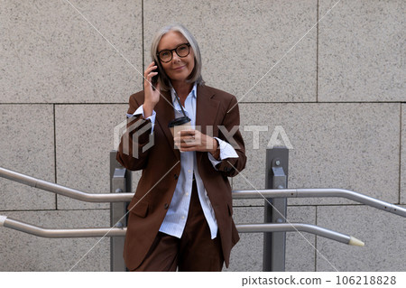 portrait of a confident successful 60 year old gray-haired business lady in glasses wearing a brown 106218828