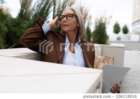 a mature woman with gray hair in a brown jacket is sitting at a table on the terrace of a cafe 106218918