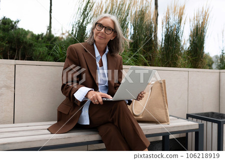 a business woman of mature years dressed in an elegant brown jacket, trousers and a shirt walks 106218919