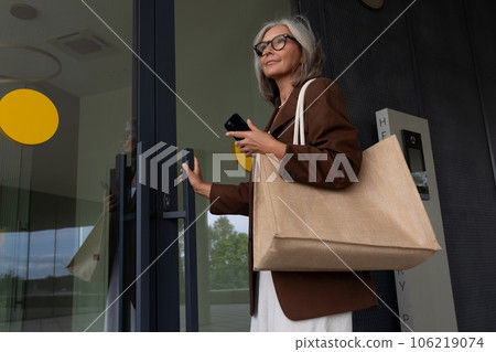 a well-groomed middle-aged woman dressed in a brown jacket enters a business building 106219074