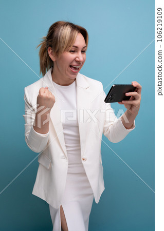 pretty young fair-haired business woman in a jacket and dress joyfully watches a video on the phone 106219109