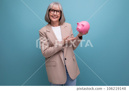 pleasant 60s middle-aged woman with a piggy bank of money on a bright background with copy space 106219148