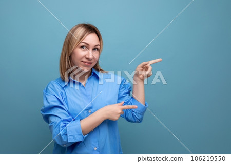 bright blond young woman in a casual shirt shows her hands to the right at a baner on a blue 106219550