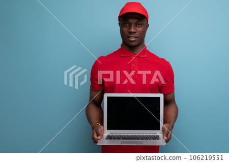 young american man dressed in a baseball cap and t-shirt uniform holding a laptop 106219551
