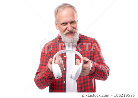 A 60-year-old gray-haired pensioner man with a beard and mustache in a shirt listens to music on 106219556