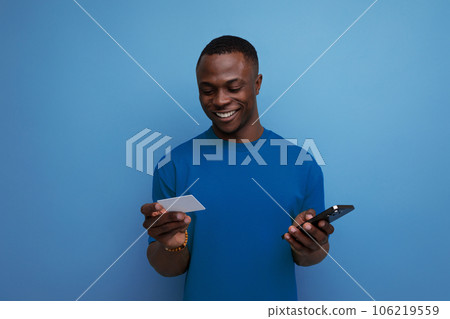 young handsome african man dressed in t-shirt uses online payments from smartphone 106219559