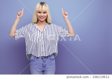smiling positive blond young woman in striped shirt pointing finger at advertisement on studio 106219612