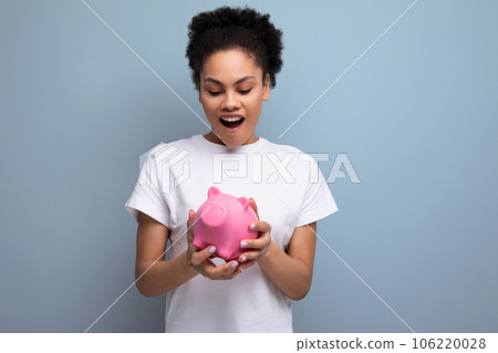 young happy hispanic brunette woman saving money for a dream in a pink piggy bank young happy hispanic brunette woman saving money for a dream in a pink piggy bank 106220028