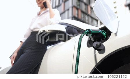 Businesswoman recharge her electric car from charging station. Peruse 106221152