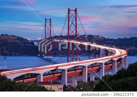 View of Lisbon view from Miradouro do Bairro do Alvito viewpoint of Tagus river, traffic with light trails on 25th of April Bridge, and Christ the King statue in the evening twilight. Lisbon, Portugal 106221373