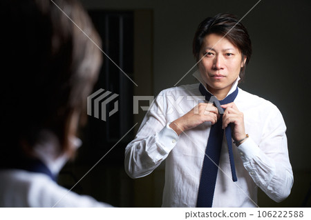 Business person tightening a tie while looking in the mirror 106222588